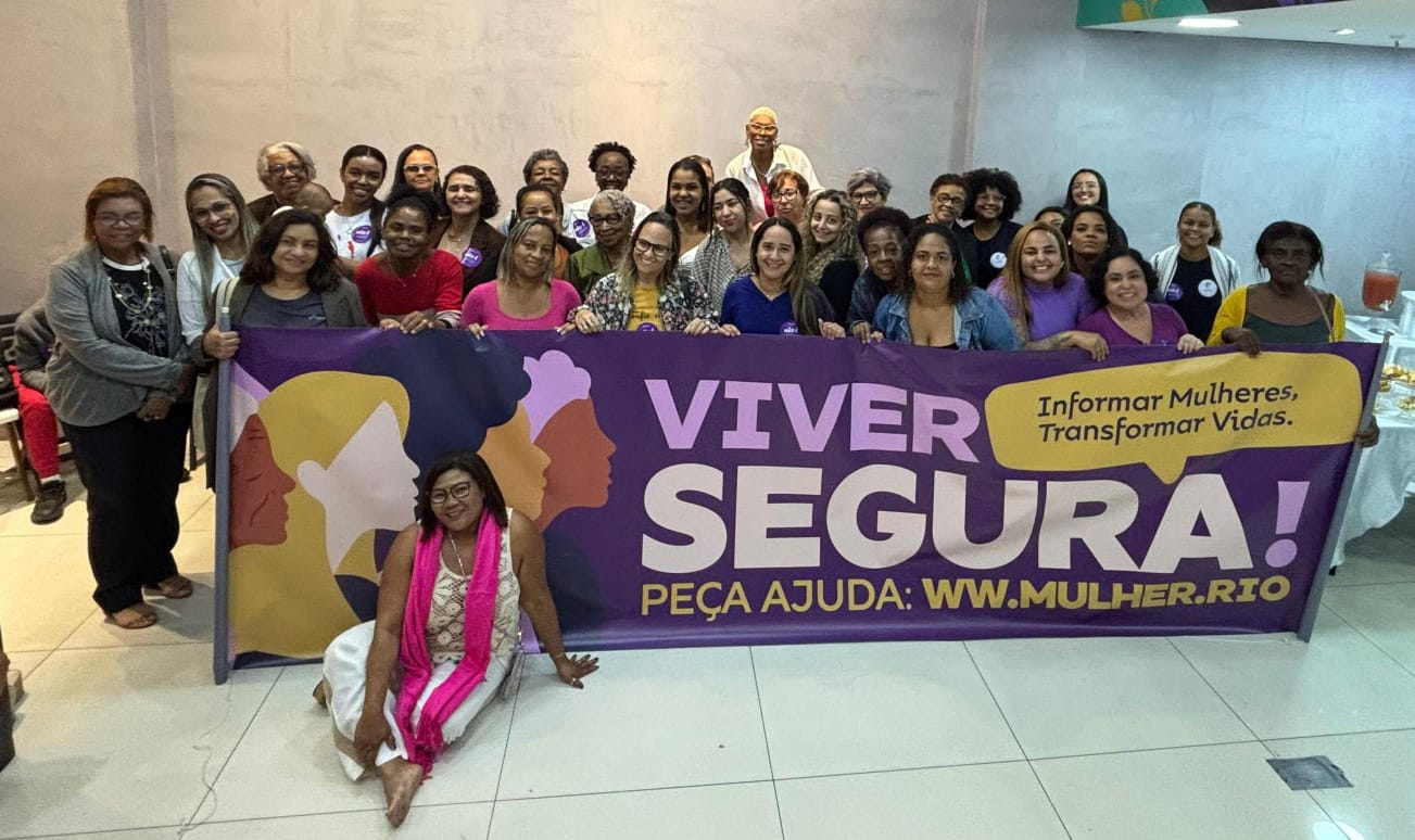 Mulheres reunidas com a faixa da campanha Viver Segura, informando mulheres e transformando vidas